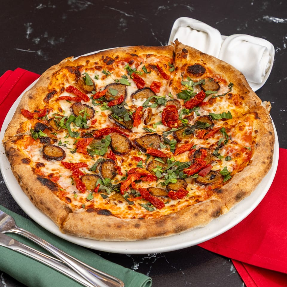 Ti Amo Wood Fired Pizza with sausage, sun-dried tomatoes, and fresh basil on a white plate.