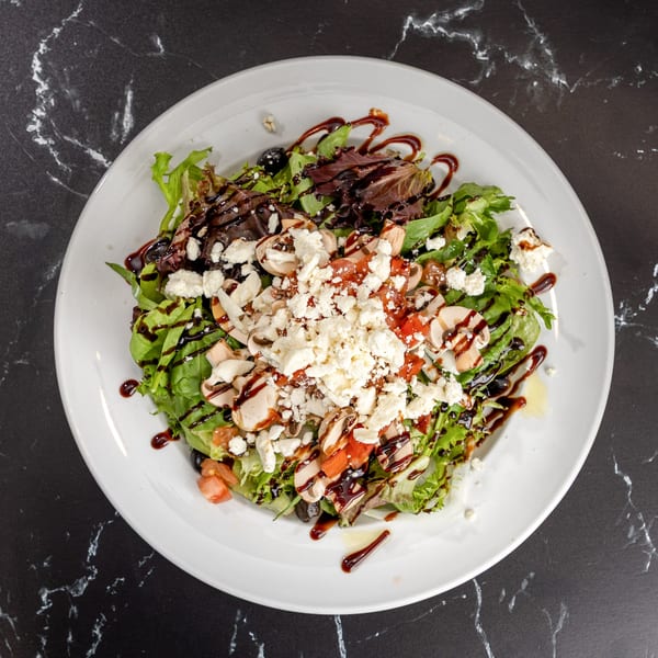 Fresh garden salad with mixed greens, tomatoes, mushrooms, feta cheese, and balsamic glaze.