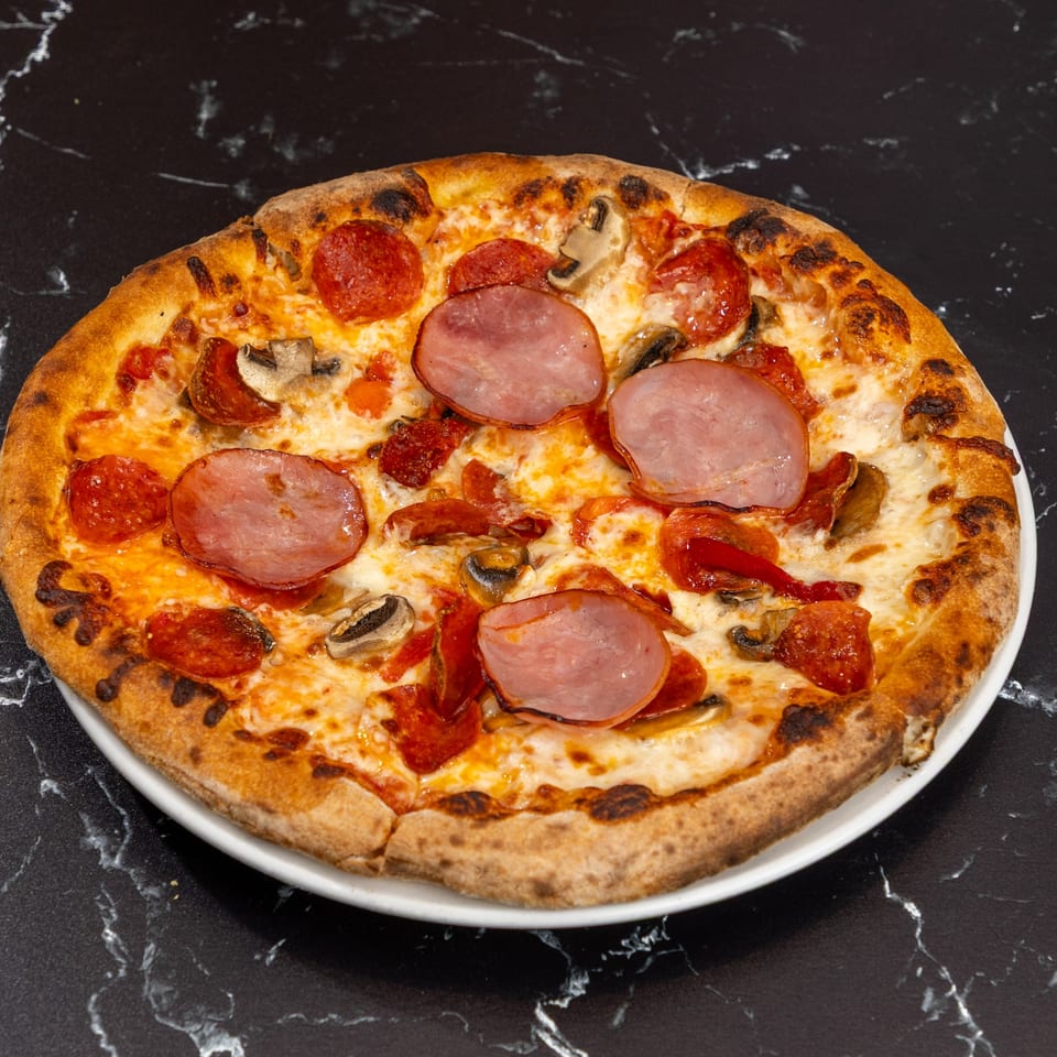 Ti Amo Wood Fired Pizza with pepperoni, ham, and mushrooms on a white plate.