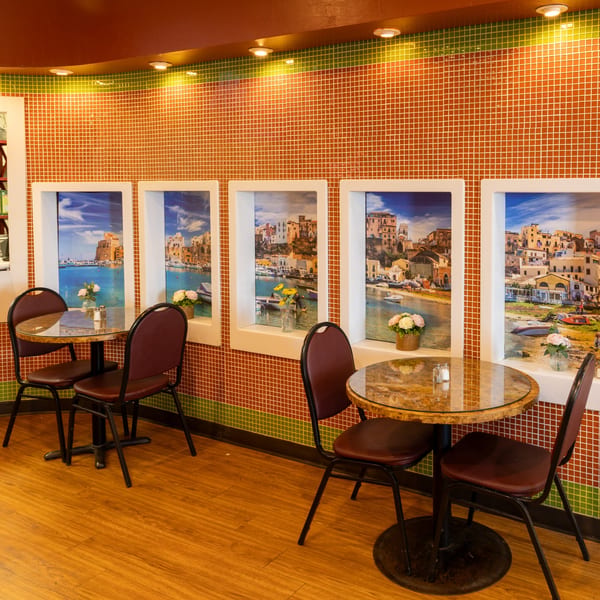 Two round tables with chairs in a restaurant with tiled walls and scenic Italian coastal prints.