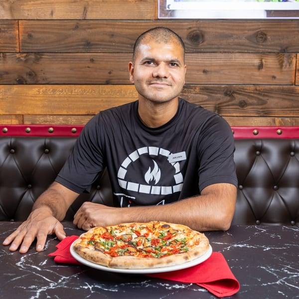 Arjan, a Ti Amo Wood Fired Pizza employee, sits at a table with a fresh pizza.