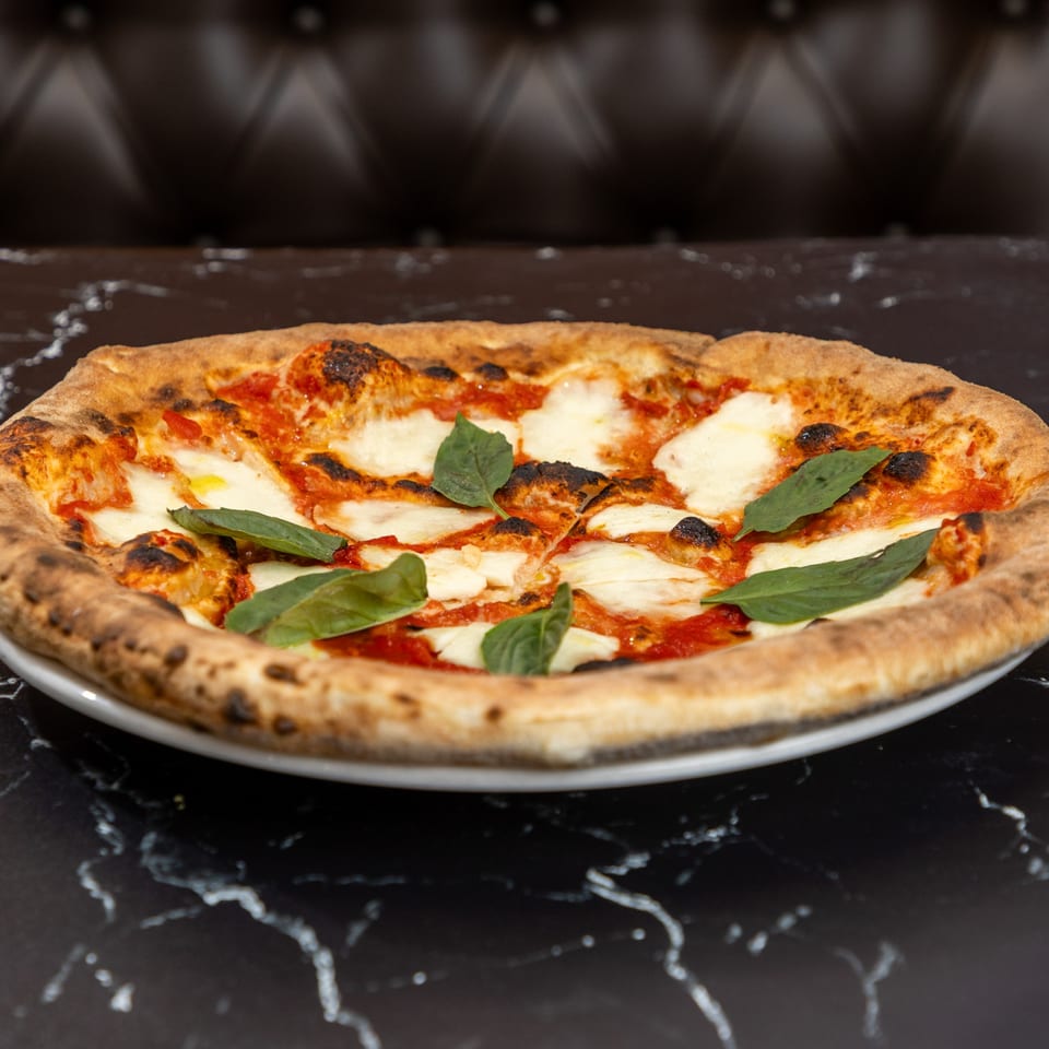 A freshly baked Ti Amo Wood Fired Pizza Margherita with basil leaves on a white plate.