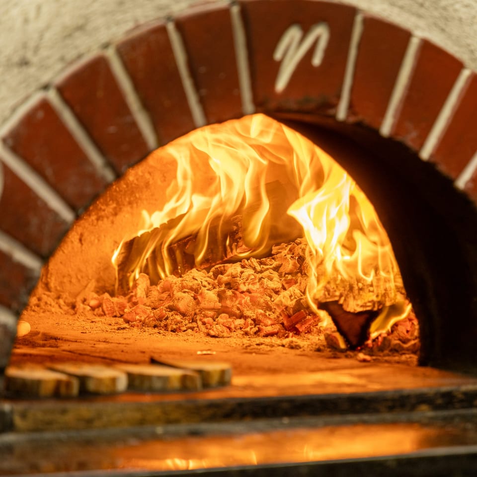 Flames and glowing embers inside a brick wood-fired pizza oven at Ti Amo.