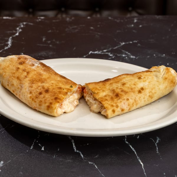 A golden-brown calzone, sliced in half to reveal melted cheese and sauce, on a white plate.