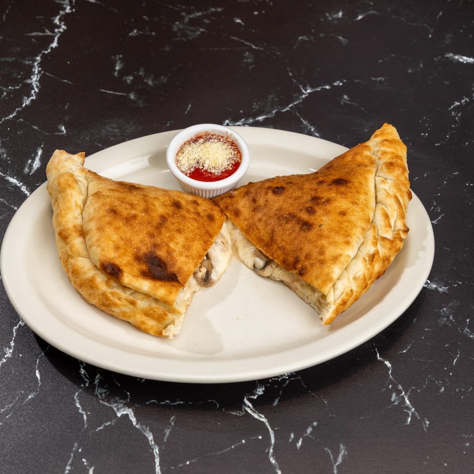 Two golden-brown calzones, cut open to reveal melted cheese and mushrooms, with a side of marinara.