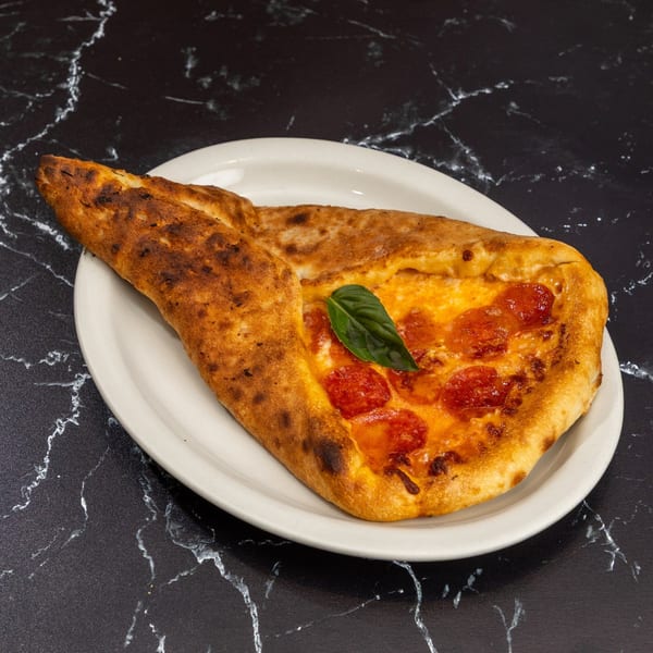 A calzone with pepperoni, melted cheese, and a basil leaf on a white plate.