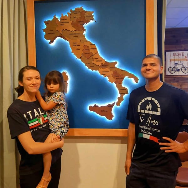 Family posing in front of a large, illuminated wooden map of Italy at Ti Amo Wood Fired Pizza.