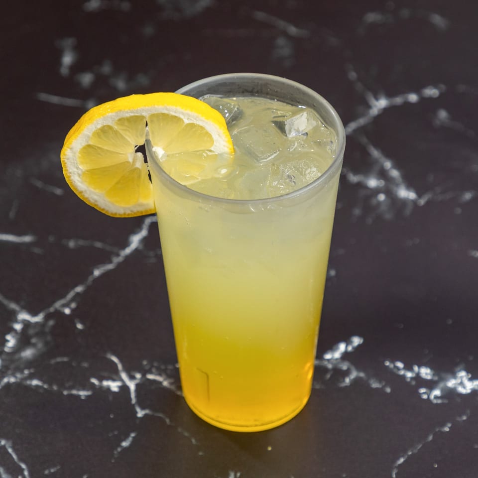 A refreshing glass of lemonade with ice and a lemon slice on a dark marble surface.