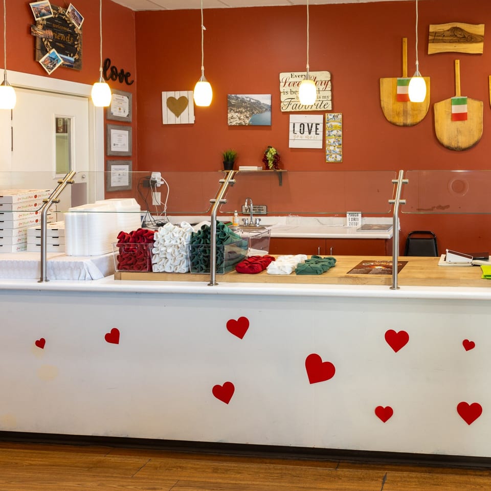 Ti Amo Wood Fired Pizza counter with pizza boxes, red and green napkins, and heart decorations.