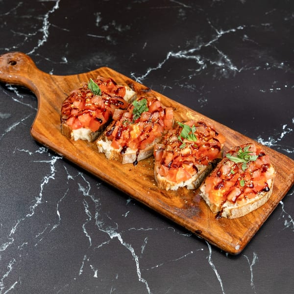 Four bruschetta with diced tomatoes, basil, and balsamic glaze on a wooden board.