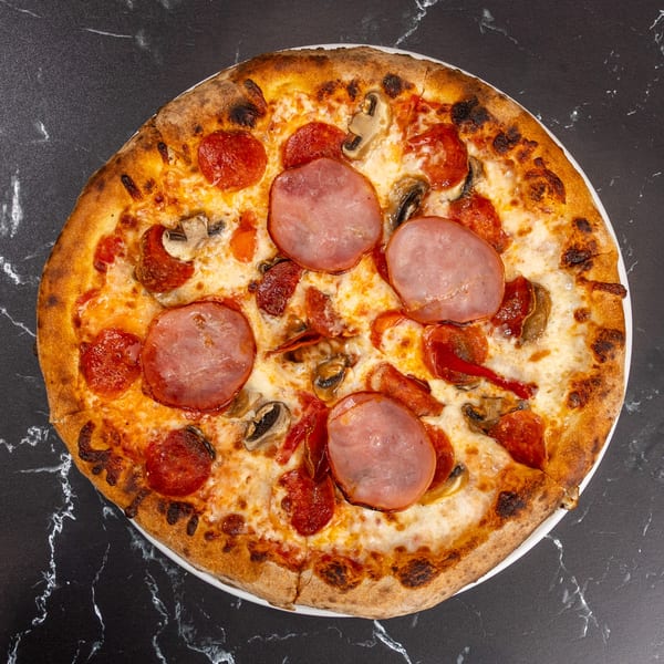 Ti Amo Wood Fired Pizza with pepperoni, ham, mushrooms, and red peppers on a dark marble surface.