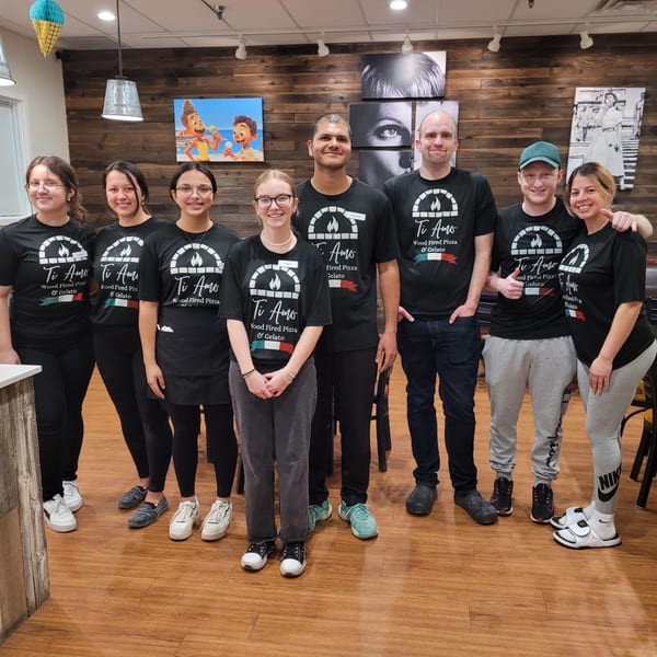 Eight Ti Amo Wood Fired Pizza & Gelato staff members in black shirts pose in the restaurant.