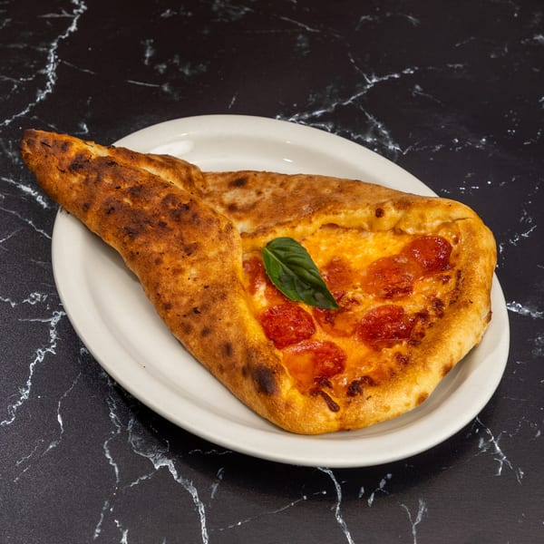 A pepperoni pizza calzone with a basil leaf on a white plate, against a black marble background.