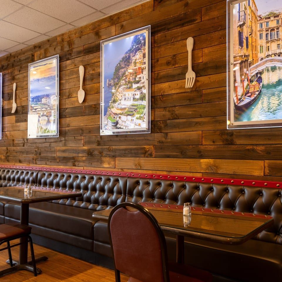 Restaurant interior with dark brown booths, wooden walls, and framed Italian landscape pictures.