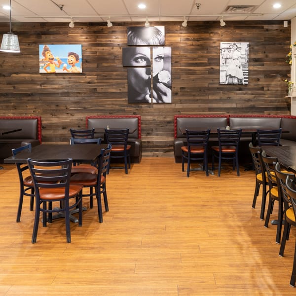 Empty dining room with dark tables, blue chairs, and brown booths against a wood-paneled wall.