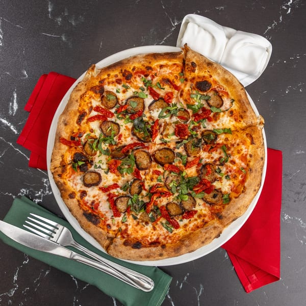 Ti Amo Wood Fired Pizza with sausage, sun-dried tomatoes, and basil on a dark marble table.