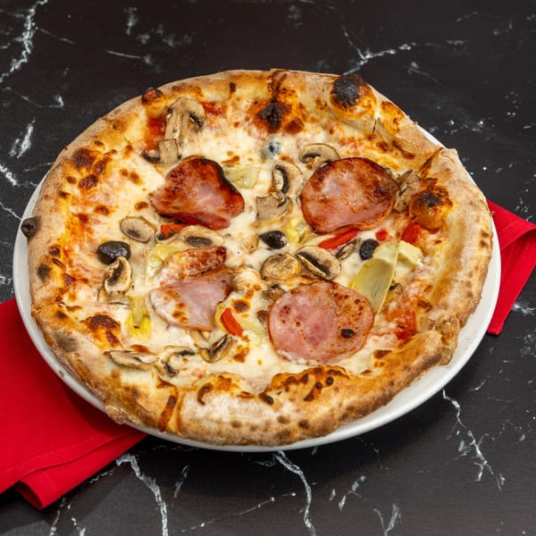 Ti Amo Wood Fired Pizza with ham, mushrooms, olives, and artichoke hearts on a black marble surface.