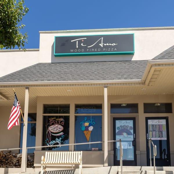 Exterior of Ti Amo Wood Fired Pizza restaurant with a sign, windows, and an American flag.
