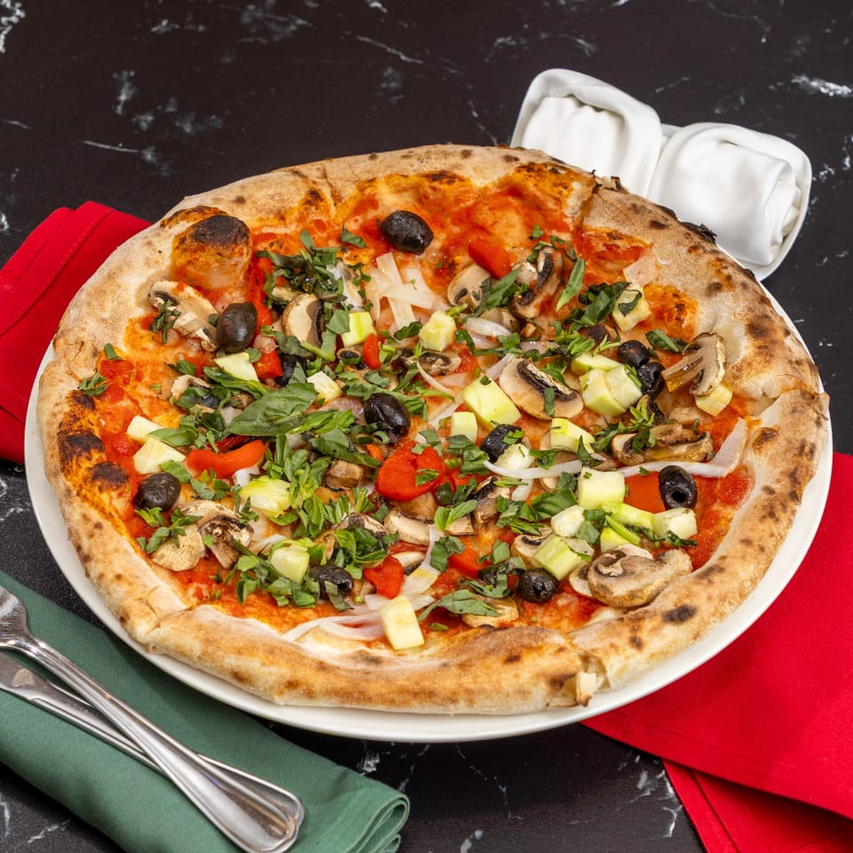 Ti Amo Wood Fired Pizza's vegetarian pizza with mushrooms, olives, peppers, and zucchini on a white plate.