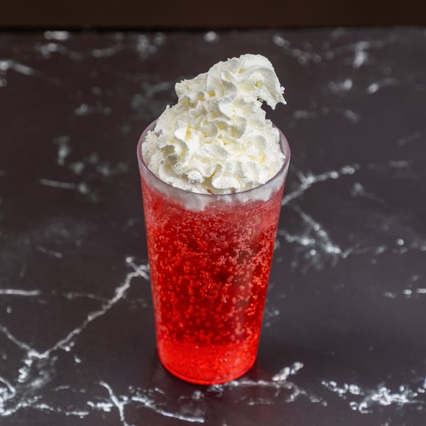 A vibrant red, bubbly drink topped with a generous swirl of white whipped cream on a dark marble surface.